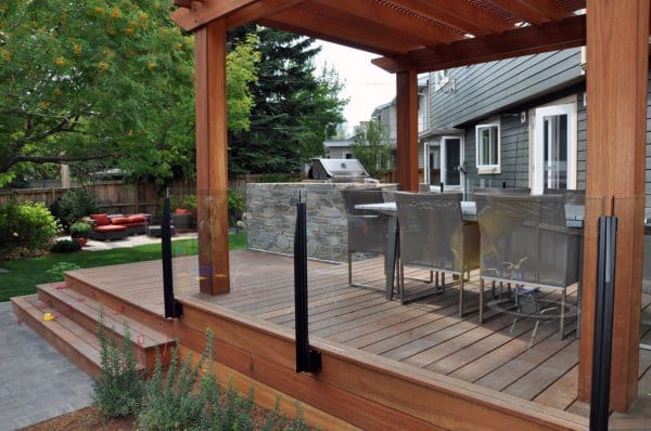 Wooden deck with pergola, glass railing, outdoor dining area, and landscaped backyard.