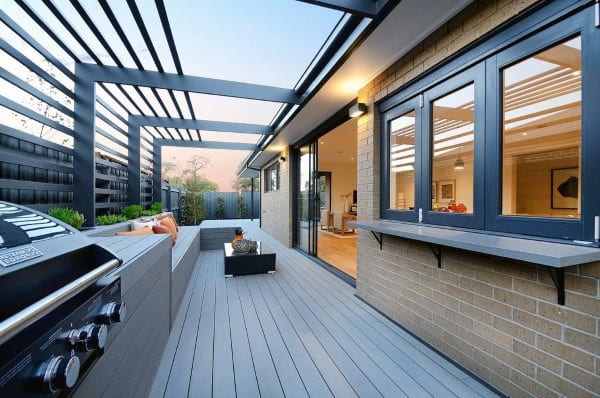 Modern pergola deck with built-in seating, grill area, and sliding windows connecting indoors.