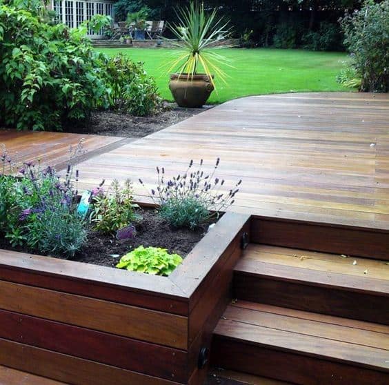 Wooden deck with built-in planter boxes, steps, and lush garden view.