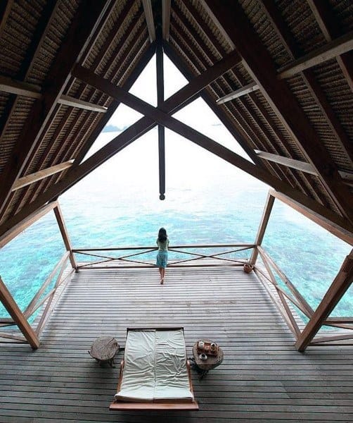 Wooden deck overlooking turquoise water with a person standing and a lounge chair.