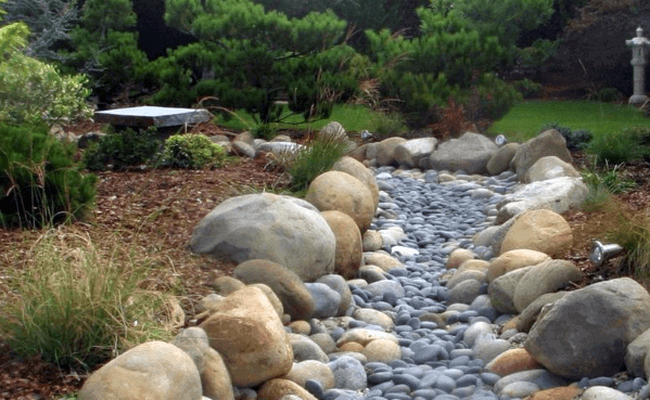 Serene river rock landscaping with large smooth stones forming a natural stream, surrounded by plants and trees