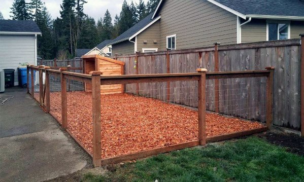Enclosed backyard area with a wooden fence and a small shelter on mulch ground