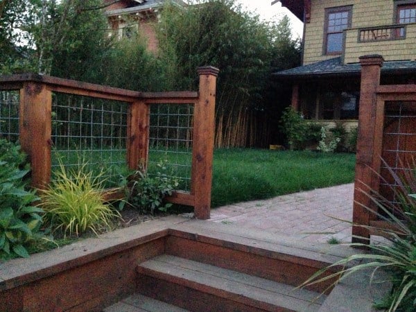 Wooden backyard fence with wire mesh panels, surrounding a grassy lawn and garden steps.