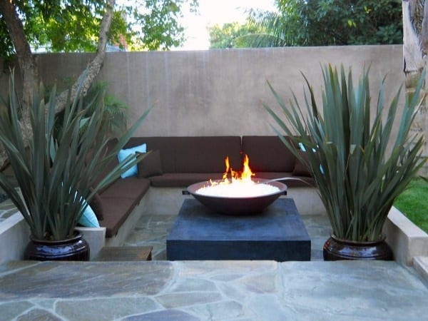 Outdoor patio with a cozy fire pit, surrounded by brown seating and tall green plants