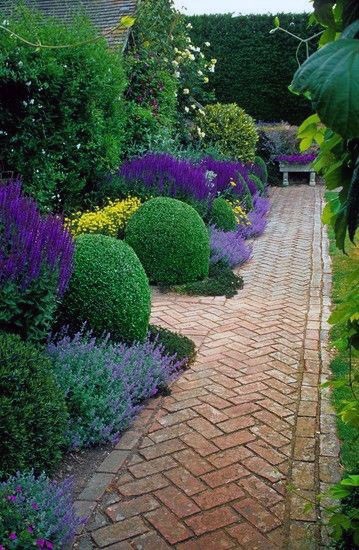 Charming brick walkway bordered by lush greenery and vibrant purple and yellow flowers, creating a serene garden path