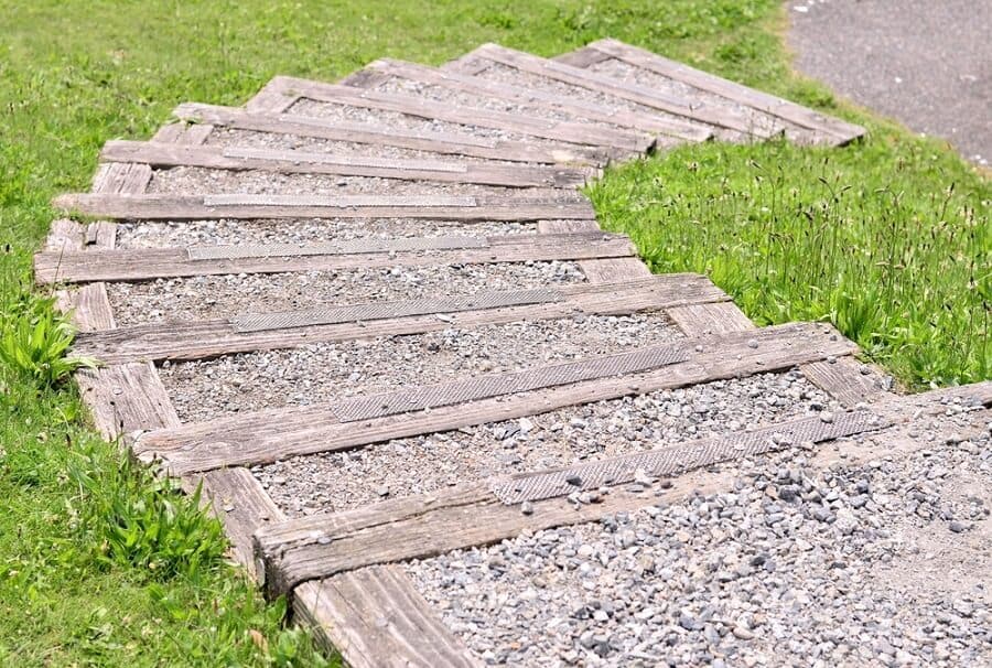 Gravel-lined wooden walkway descends through a grassy area
