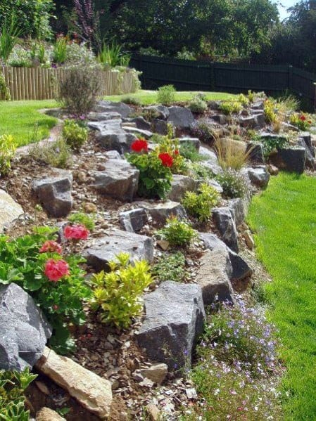 Backyard slope landscaping with large boulders, colorful flowers, and green shrubs creating a natural and vibrant hillside design