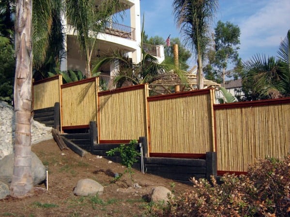 Stepped bamboo fence with wooden frame along a sloped backyard with tropical plants.