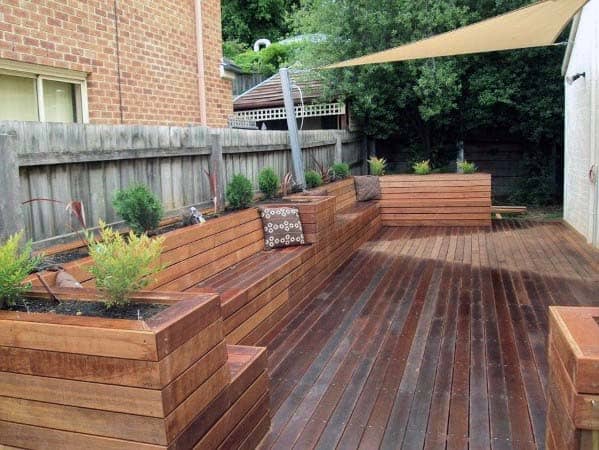 Wooden deck with raised planters and bench seating, surrounded by a fence and shaded by a canopy
