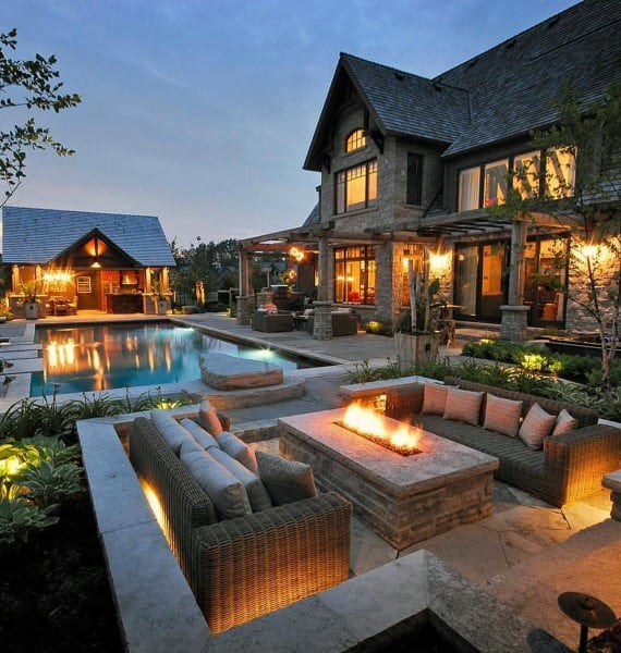 Luxurious house with pool and patio featuring an outdoor seating area around a fire pit at dusk