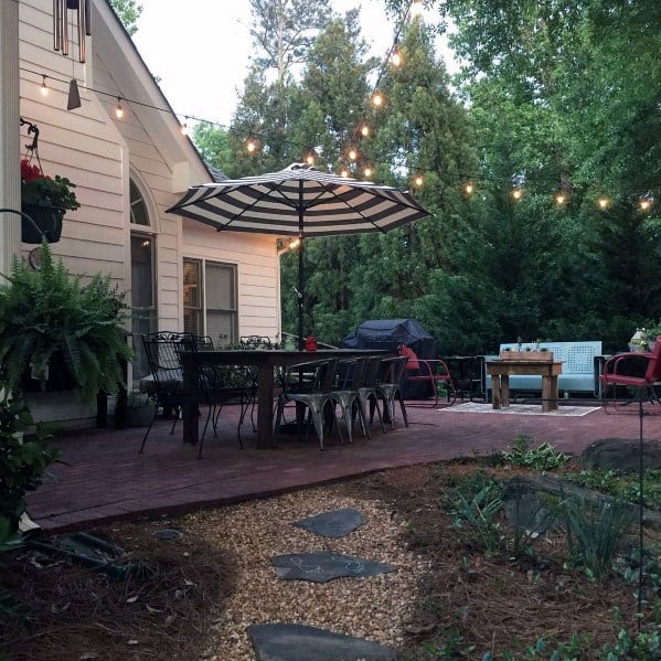 Cozy backyard patio with string lights, brick seating area, umbrella, and surrounding trees