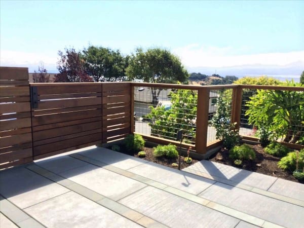 Modern wooden fence with wire mesh panels surrounding a landscaped patio area with scenic views.