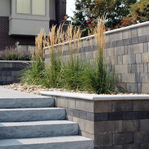 Modern stone retaining wall with built-in planter, ornamental grasses, and adjacent steps.