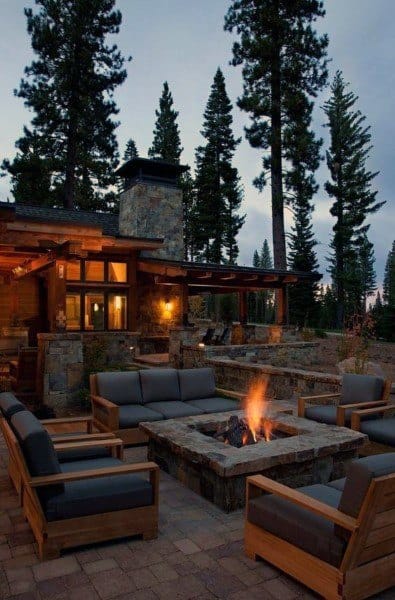 Cozy outdoor seating with a fire pit, nestled among pine trees and a rustic cabin at dusk