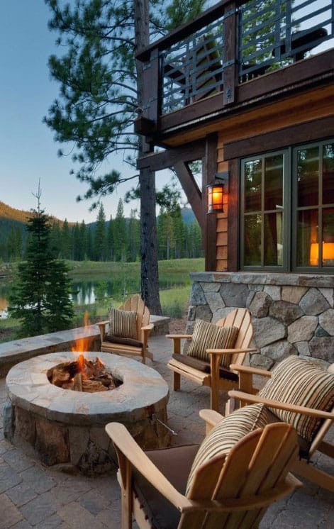Cozy outdoor patio with a fire pit, surrounded by wooden chairs and a view of trees and a lake in the background