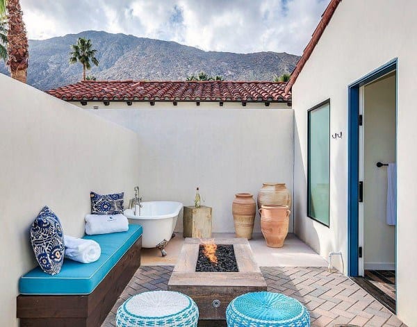 Rustic patio with a blue daybed, freestanding bathtub, fire pit, mountain view, and pottery accents
