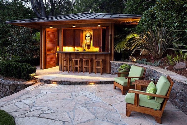 Outdoor pavilion bar with wooden stools, tropical decor, and comfortable seating on a stone patio.