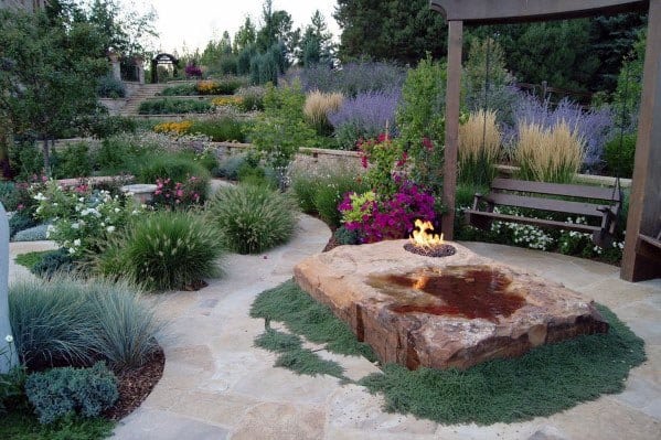 Elegant patio design on a sloped yard with a fire pit, vibrant flowers, layered greenery, and a serene garden bench area