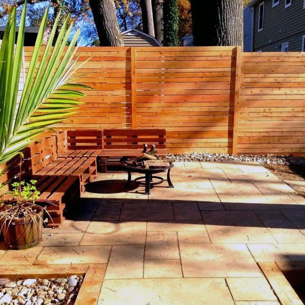 Sunny patio with wooden benches, a small table, potted plant, and a rustic fence in the background