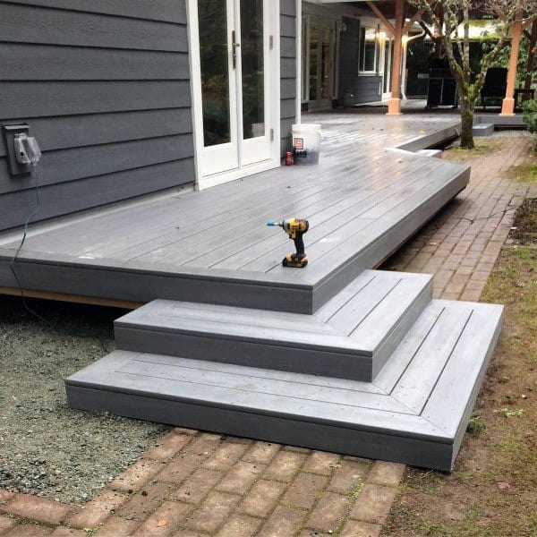 Gray wooden deck with steps, brick pathway, and modern exterior setting.