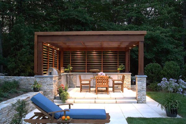 Modern flat-top pavilion with a dining area, stone accents, and lounge chair in a serene backyard.