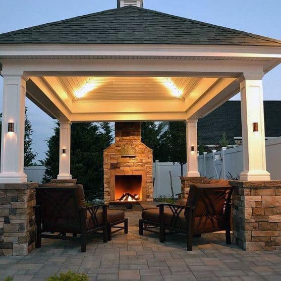 Stone pavilion with outdoor fireplace, cozy seating, and soft lighting, creating a warm evening ambiance.