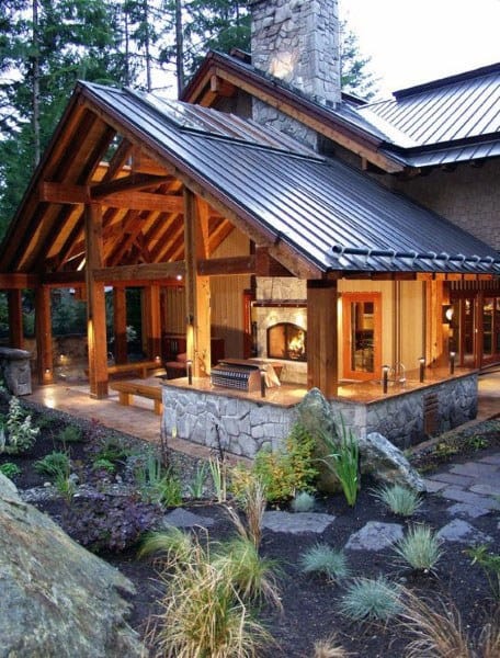 Rustic timber pavilion with stone accents, open seating, and fireplace, set in a landscaped garden.