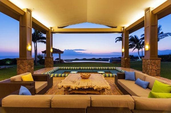 Open-air stone pavilion with comfortable seating and ocean view at sunset, featuring natural decor.