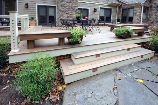 Backyard platform deck with built-in benches, potted plants, and stone patio steps.