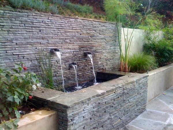 Modern backyard pond with a stacked stone wall and cascading water features.