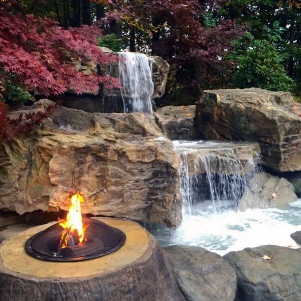 Backyard pond with cascading waterfalls and a built-in fire pit surrounded by rocks.