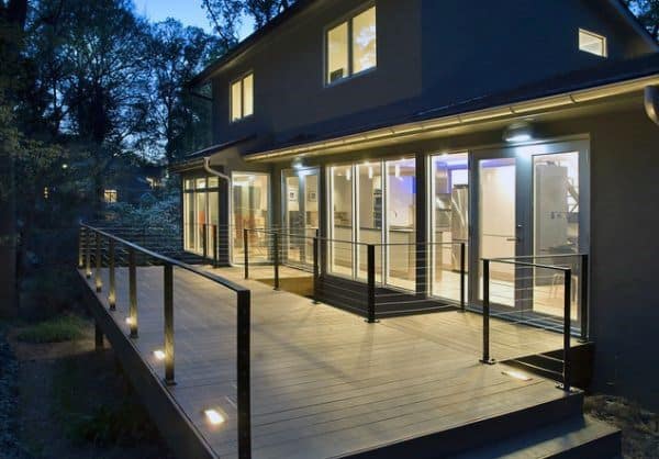 Modern elevated deck with glass railing, built-in lights, and large sliding doors at dusk.