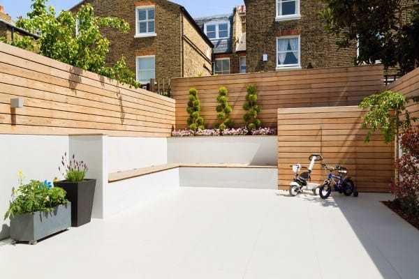 Layered horizontal wooden fence surrounding a modern backyard with planters and children's bikes.
