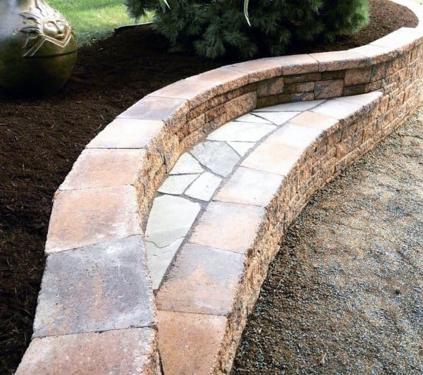 Curved stone retaining wall with built-in bench and a decorative pathway.