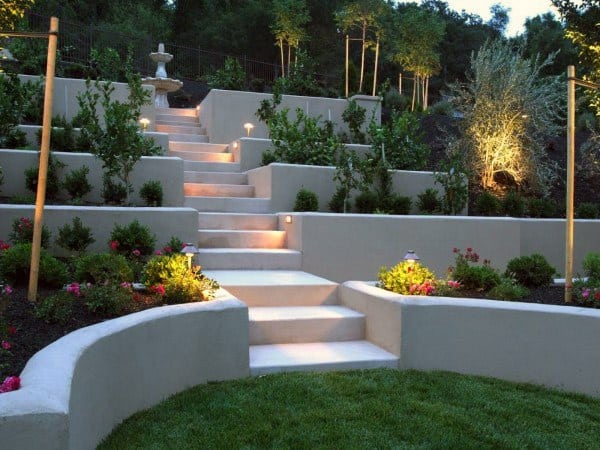 Tiered concrete retaining walls with built-in lighting, stairs, landscaped plants, and a fountain.