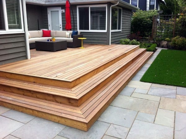 Tiered wooden deck with outdoor seating, red umbrella, and adjacent green lawn.