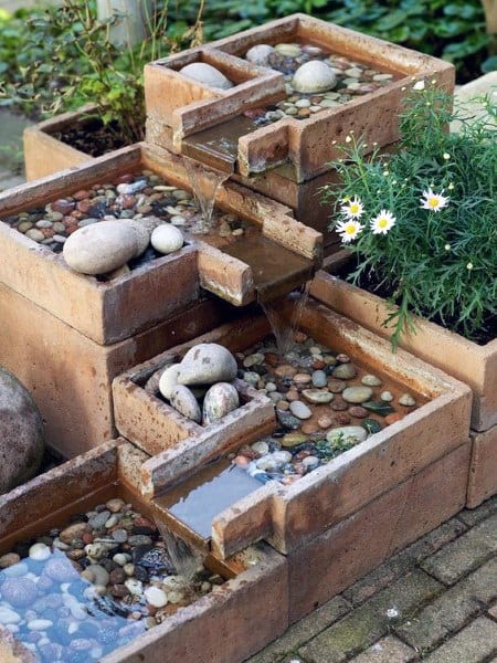 Tiered terracotta waterfall feature with smooth pebbles and flowing water for a natural look.
