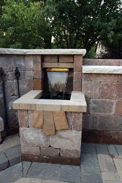 Compact backyard waterfall feature with stone masonry and a modern spout design.