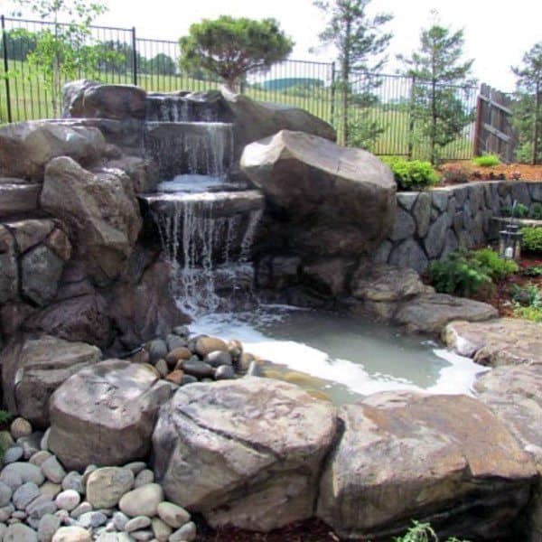 Backyard waterfall with large natural rocks and a small pond surrounded by greenery.