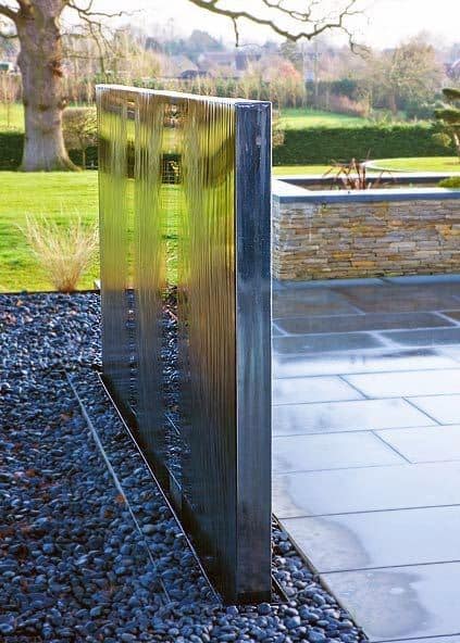 Modern stainless steel waterfall feature with sleek design and black pebble base.