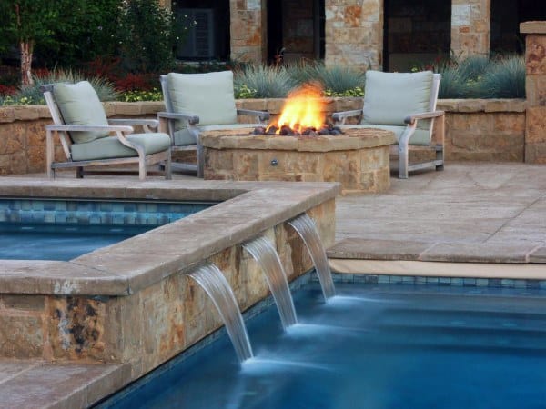 Backyard pool with cascading waterfalls, fire pit, and cozy seating area with stone accents.