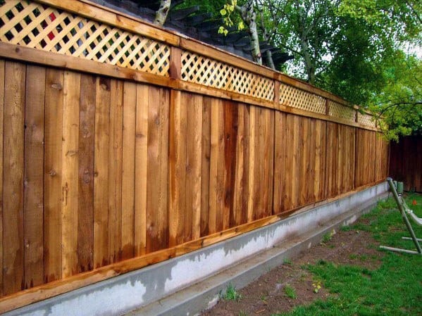 Wooden fence featuring a lattice top, lining a grassy area with trees in the background