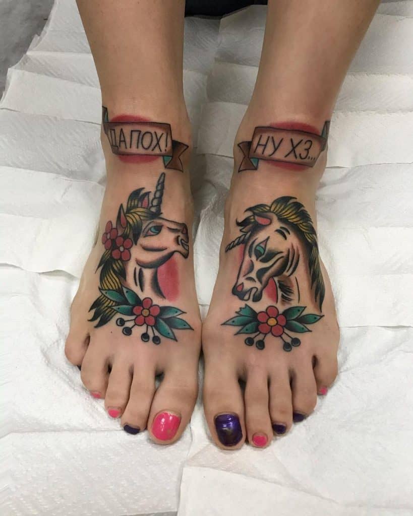 Traditional-style foot tattoos of two unicorns with floral accents, bold outlines, and vibrant colors, paired with banner text on the ankles.