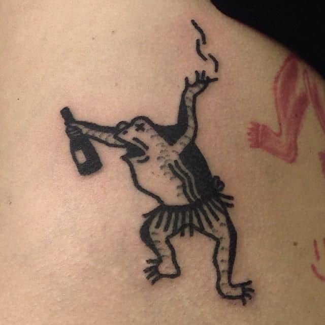 A black ink tattoo of a dancing frog wearing a skirt, holding a bottle, and exhaling smoke, drawn in a playful and tribal-inspired style.