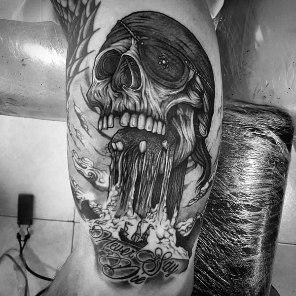 Black and gray tattoo of One-Eyed Willy from The Goonies, featuring a skull with an eye patch, a pirate ship, and the phrase "Never Say Die".