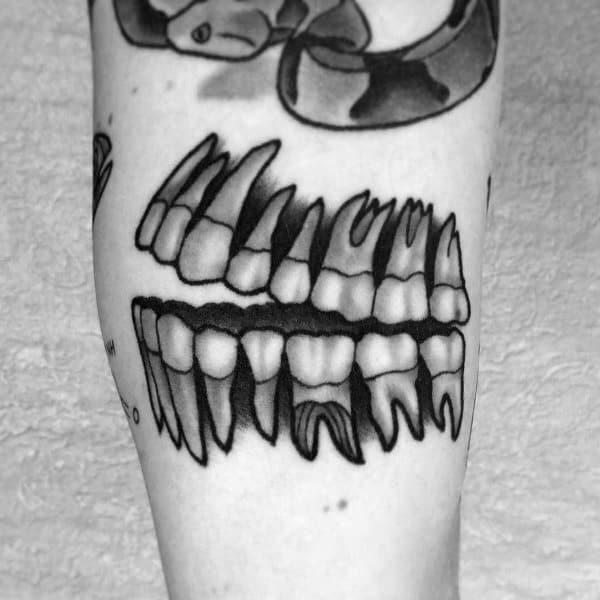 Black and grey tattoo of upper and lower jawbones with sharp teeth, stylized with bold lines and shadow for a dramatic effect.