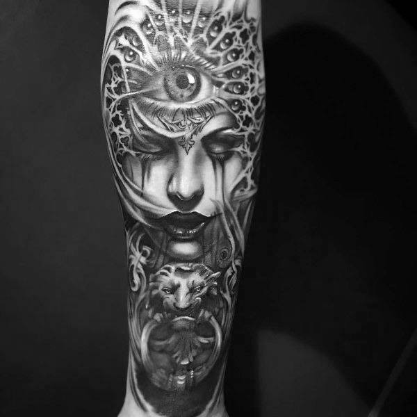 Black and grey forearm tattoo featuring a mystical woman with a third eye, intricate patterns, and a lion for a surreal and gothic aesthetic.