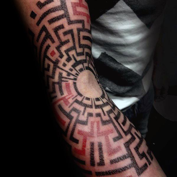 Intricate black and red labyrinth tattoo on a man's arm, radiating outward from the elbow with bold geometric patterns and maze-like paths.