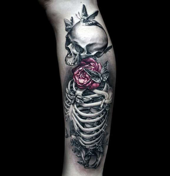 Realistic black and grey tattoo of a skeleton with a vibrant red rose and butterflies, symbolizing life and mortality on the leg.