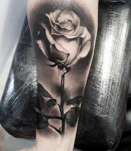 A realistic black and white rose tattoo elegantly winds its way up the forearm, with intricate details capturing every petal and the delicate curve of its stem